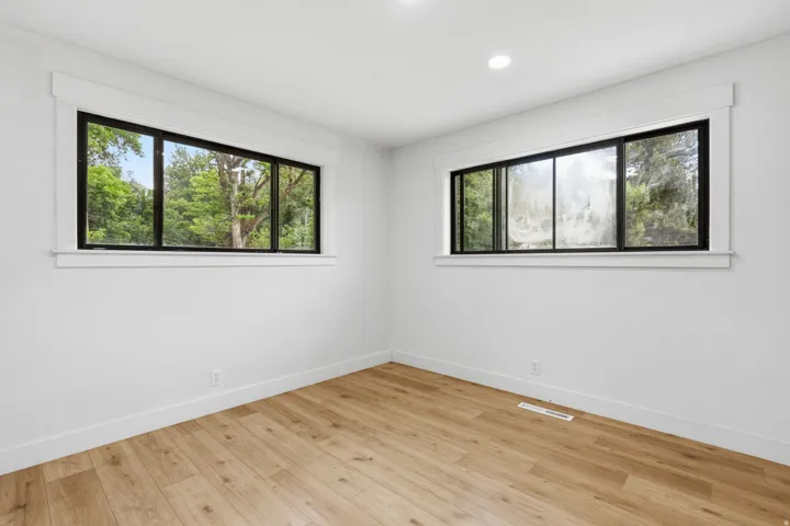 Bright interior space featuring wood-finish flooring, white baseboards, and two windows with black frames