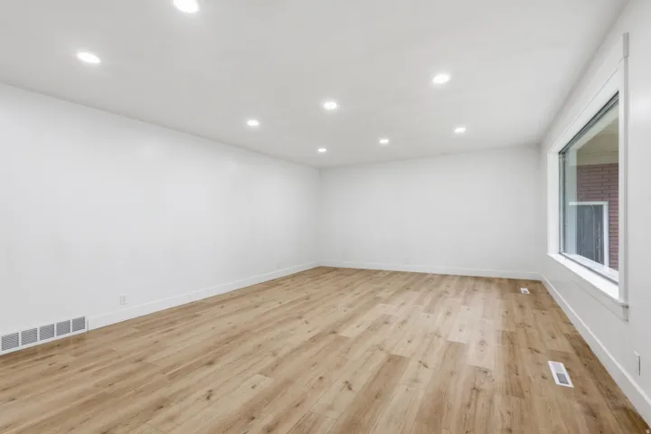 Spacious room featuring wood-finish flooring, recessed ceiling lighting, crisp white walls, white baseboards, and a large window with white trim