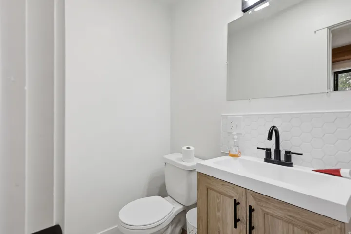 Modern bathroom featuring a wood-finish vanity with black hardware, white rectangular sink, matte black faucet, and hexagonal tile backsplash