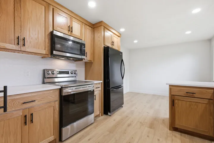 Kitchen featuring light wood-finish cabinetry, stainless steel range and microwave, black refrigerator, and light wood-finish flooring