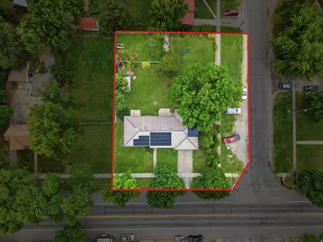 Aerial perspective showcasing a property with mature trees, a substantial grass yard, and solar panels installed on the roof