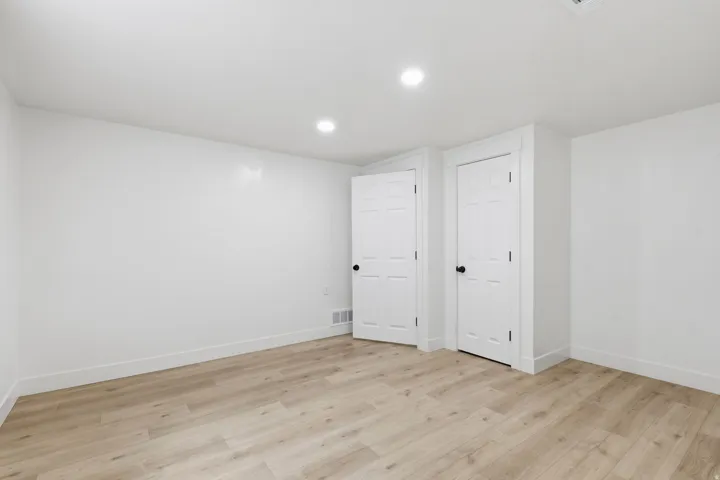 Spacious room featuring light wood-finish flooring, recessed lighting, crisp white walls, and two paneled doors with black hardware