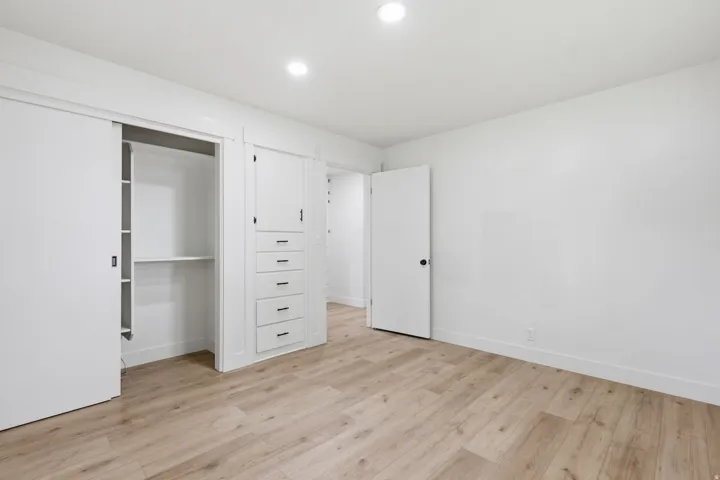 Bedroom featuring wood-finish flooring, recessed lighting, white walls, built-in closet with sliding doors, and integrated storage cabinetry with drawers