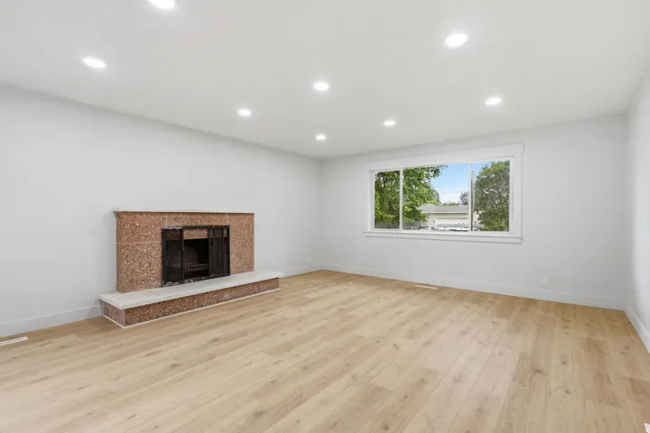 Spacious room featuring light wood-finish flooring, a fireplace with a speckled red surround and light-colored hearth, and a large window with white trim