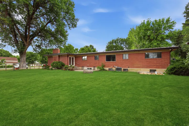 Expansive green lawn with mature shade trees, complemented by a red brick exterior, multiple windows, and a patio area