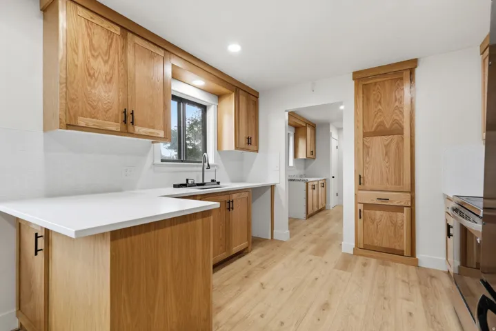 Kitchen featuring light wood cabinetry, white countertops, a stainless steel sink with a matte black faucet, and wood-finish flooring