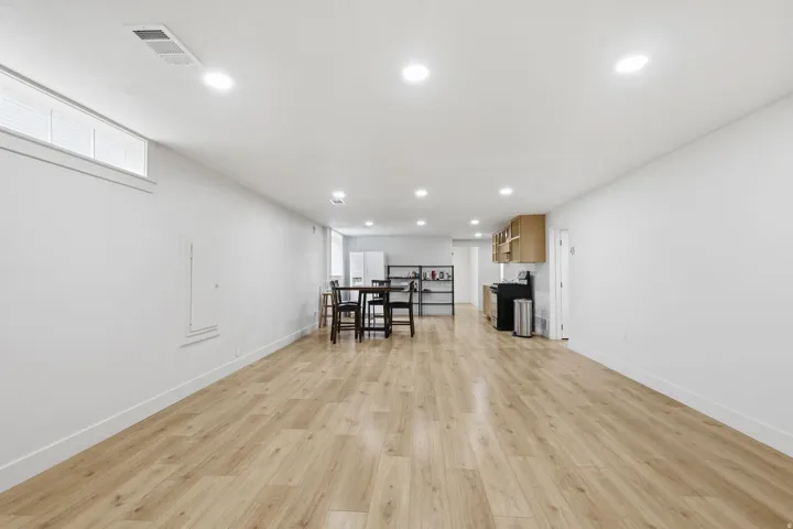 Spacious open-concept room featuring light wood-finish flooring, recessed lighting, and crisp white walls