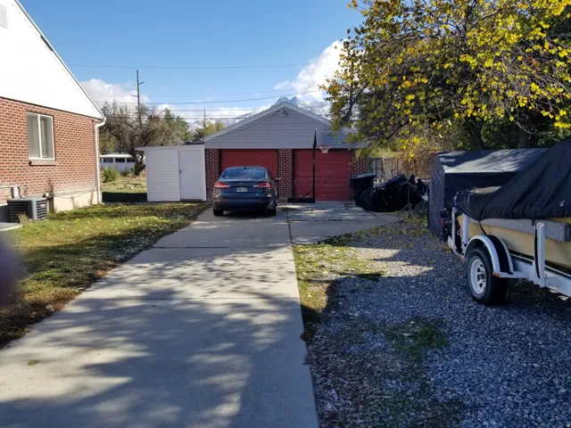 Detached garage with red doors, a concrete driveway, and a gravel parking area