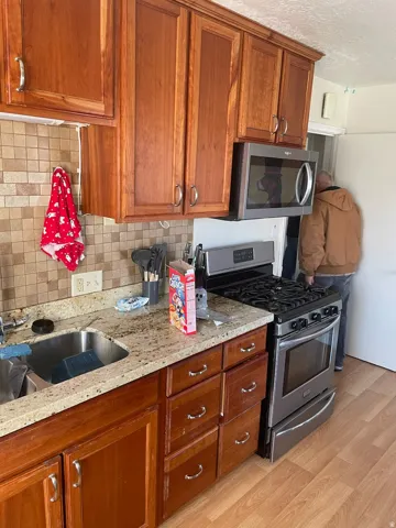 Kitchen featuring wood cabinetry, stone countertops, a stainless steel gas range, an over-the-range microwave, and a tile backsplash