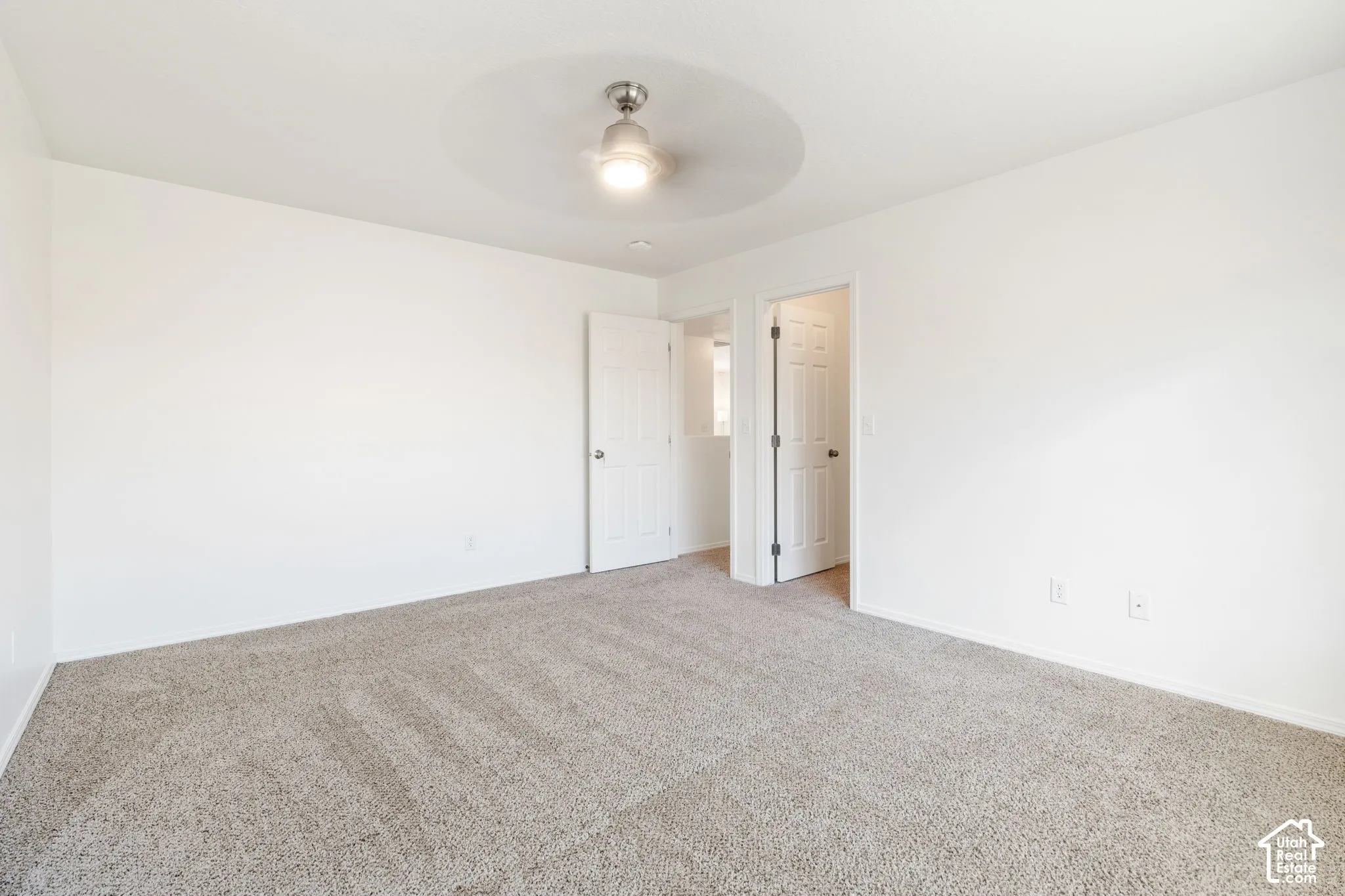 Neutral-toned carpeting paired with white walls, featuring a ceiling fan with integrated lighting