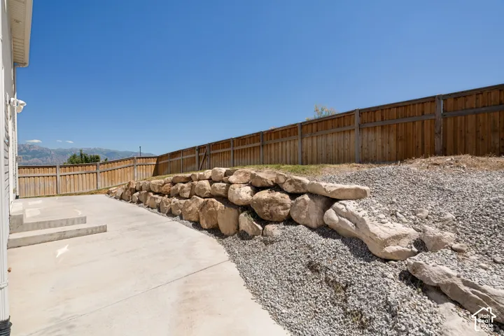 Concrete patio with multi-level steps, flanked by a natural stone retaining wall and gravel landscaping