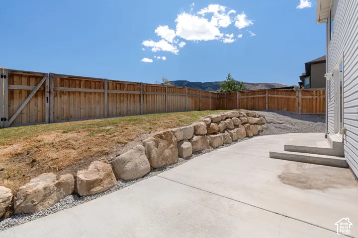 Expansive concrete patio with a natural stone retaining wall, gravel landscaping, and wood privacy fencing