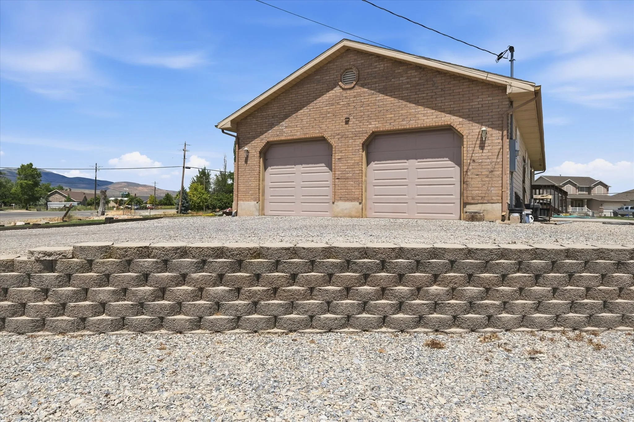 Brick-clad structure featuring dual garage doors with panel detailing, a gabled roofline, and an integrated retaining wall with modular block construction