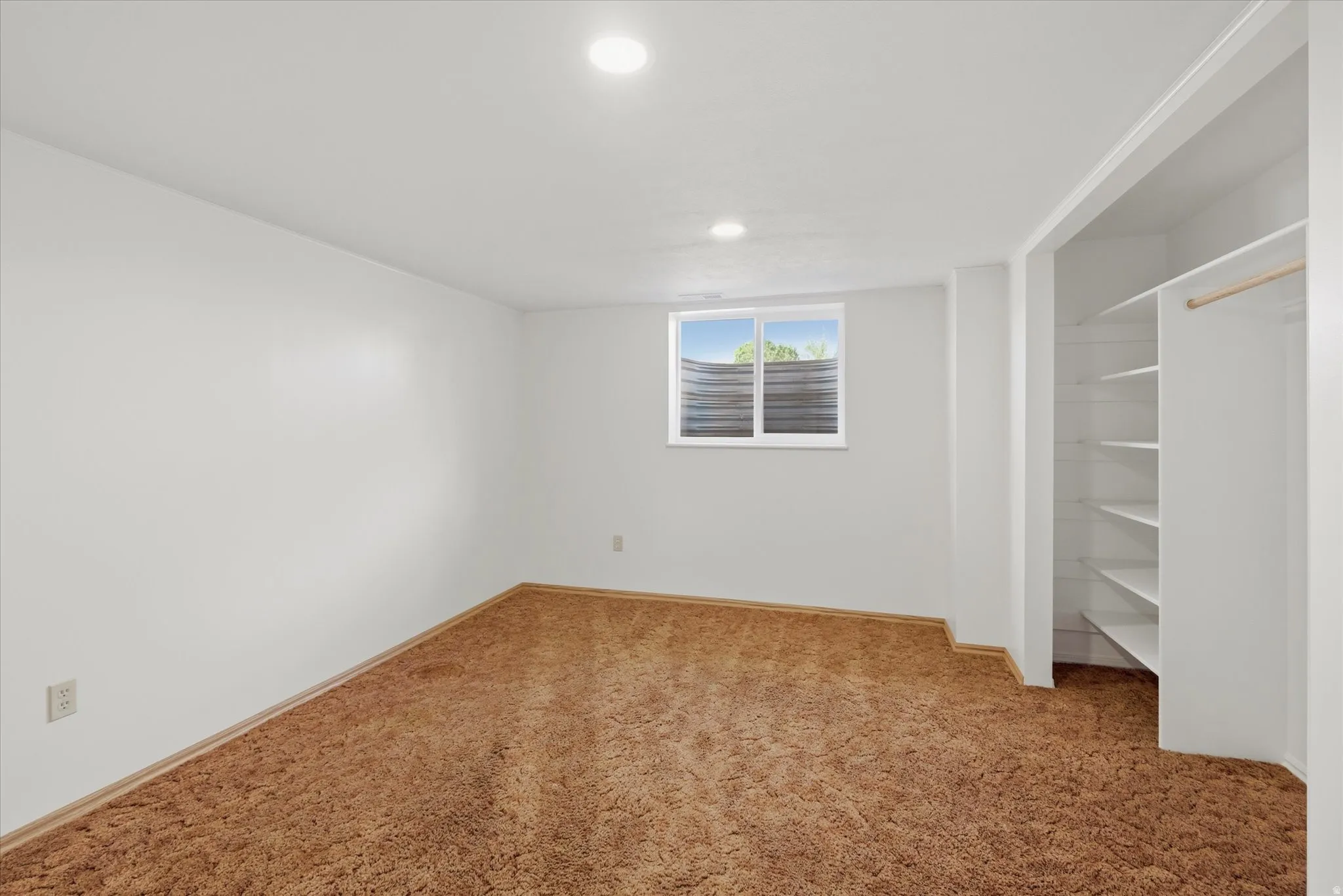 Carpeted room featuring a window with exterior light, recessed ceiling lighting, and a built-in closet with shelving and hanging rod