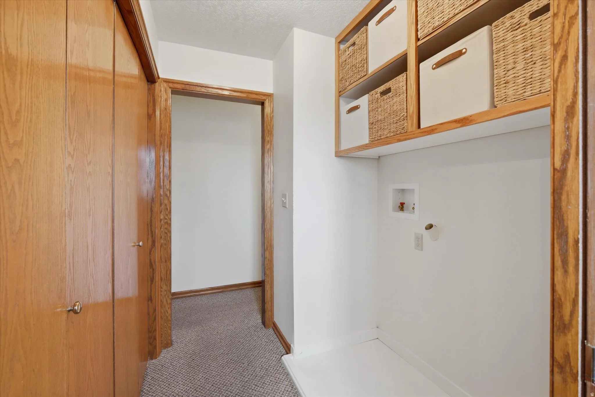Dedicated laundry alcove featuring overhead open shelving and utility connections
