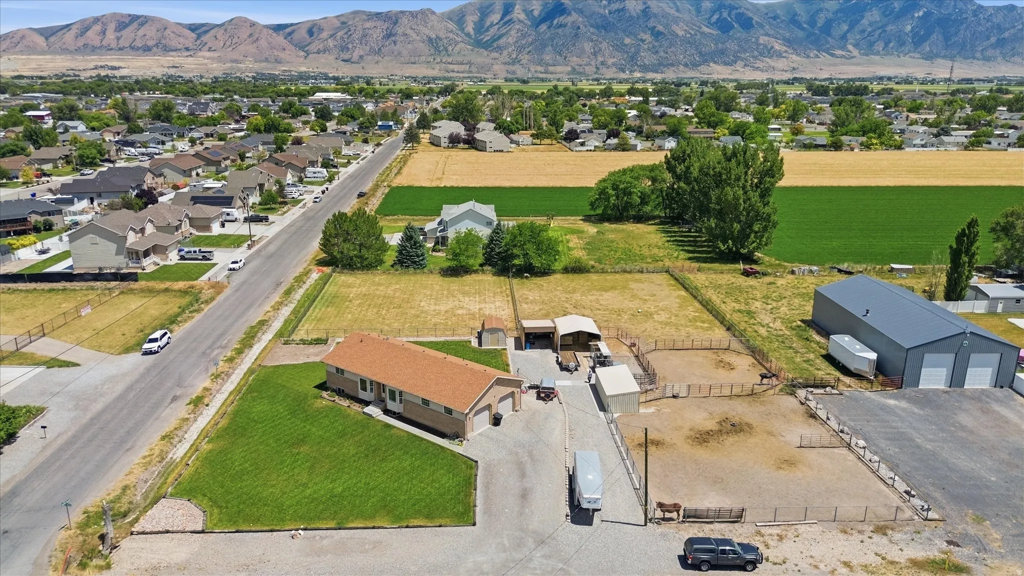 Expansive property featuring a single-story residence, a large detached metal building with multiple bay doors, and several fenced animal enclosures