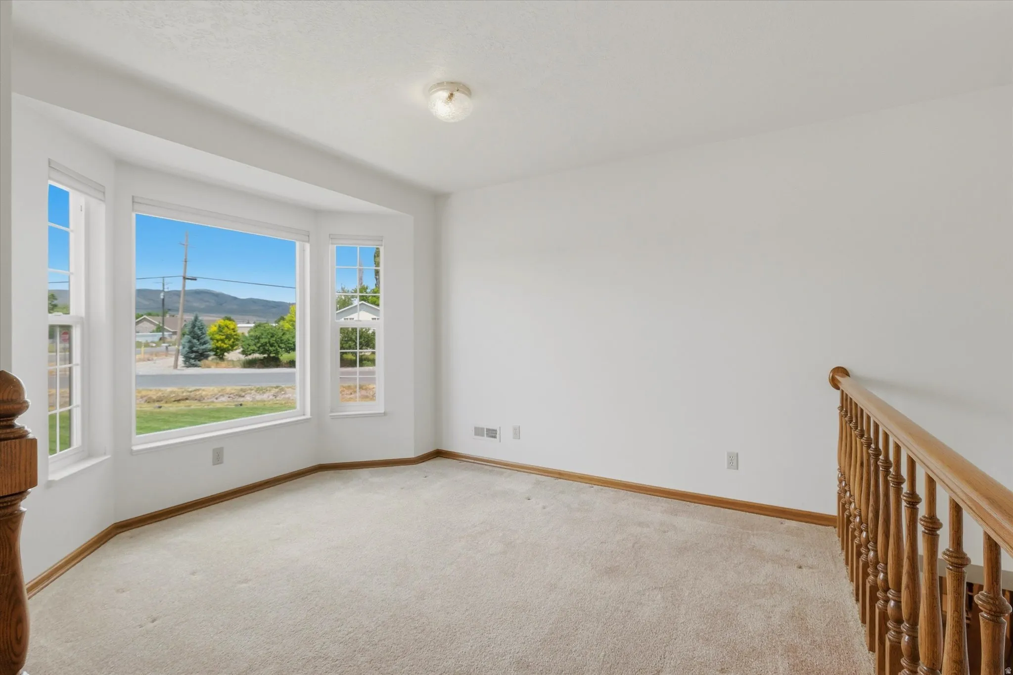Bright interior space featuring a bay window, neutral carpet flooring, white walls, and a wood-finish railing
