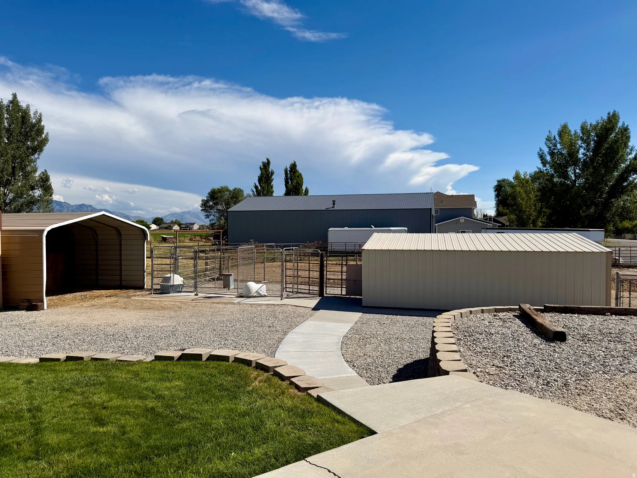Expansive exterior with a gravel and concrete patio, multiple metal outbuildings, and a grass lawn