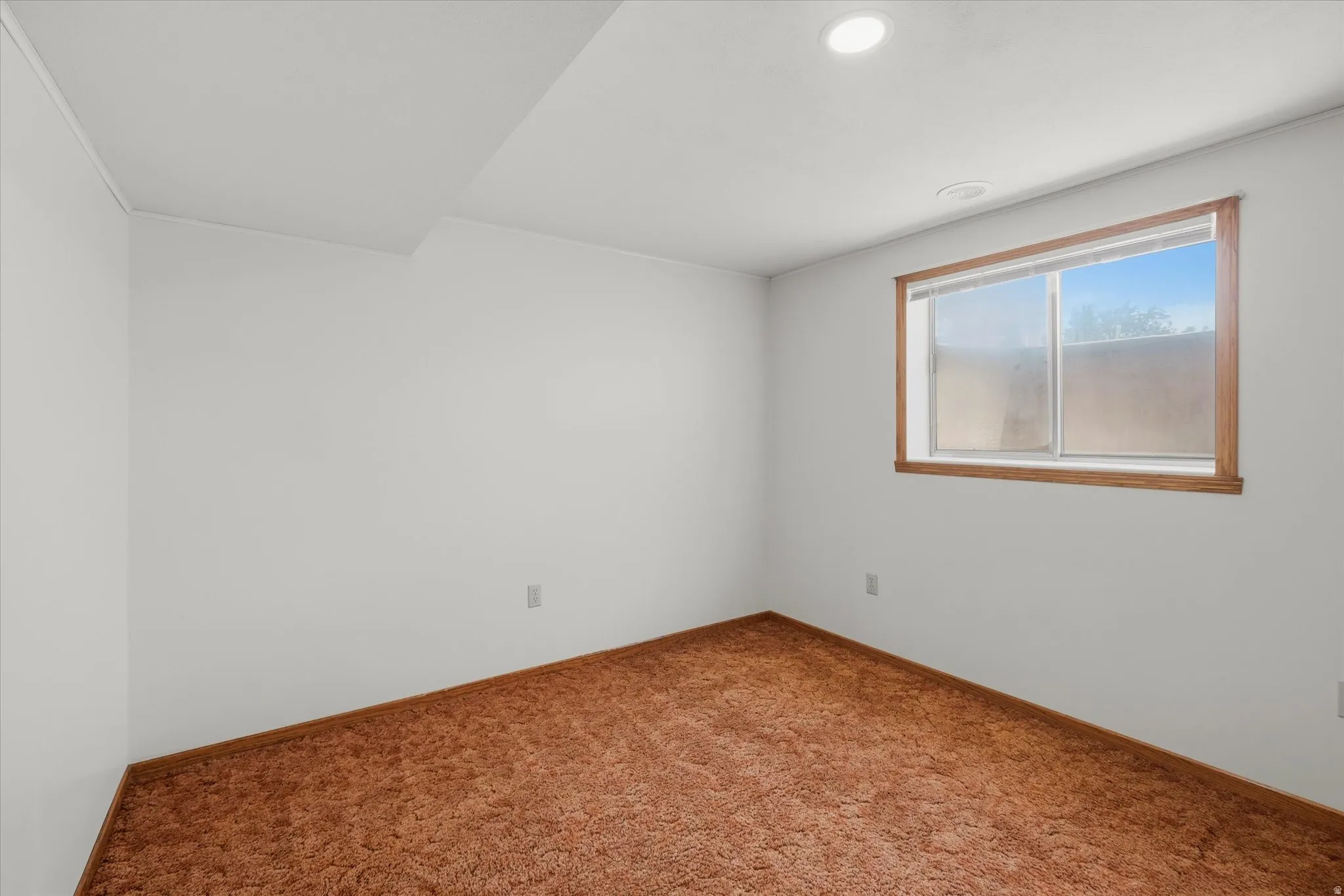Recessed lighting illuminates this room featuring white walls, brown carpet, and a wood-framed window
