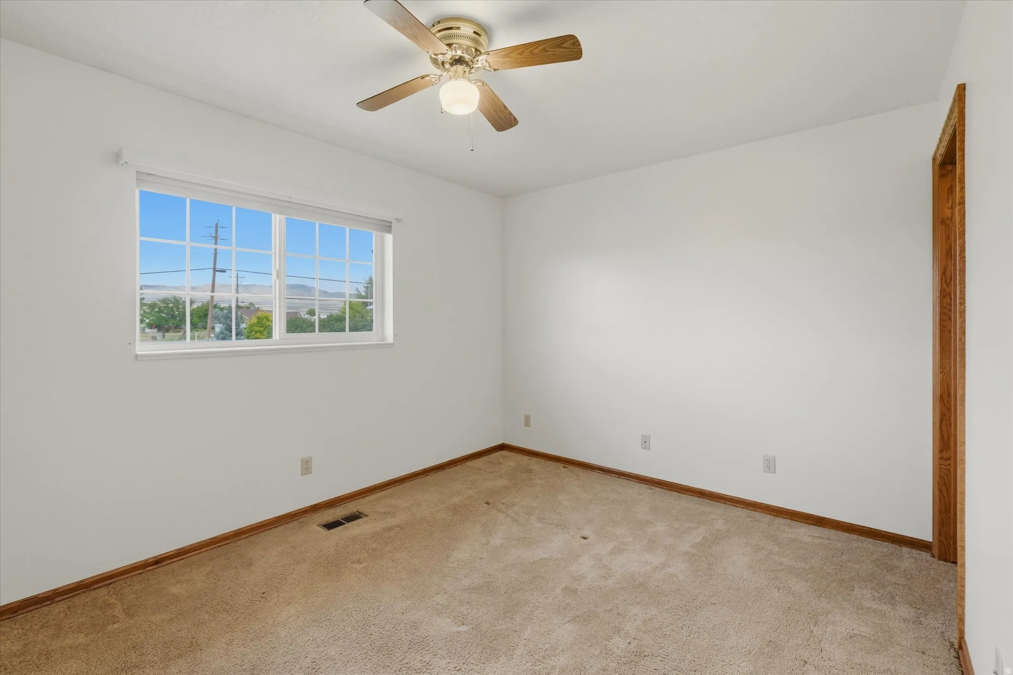Bright room featuring a multi-pane window, ceiling fan with light fixture, light-colored carpeting, and white walls with wood trim