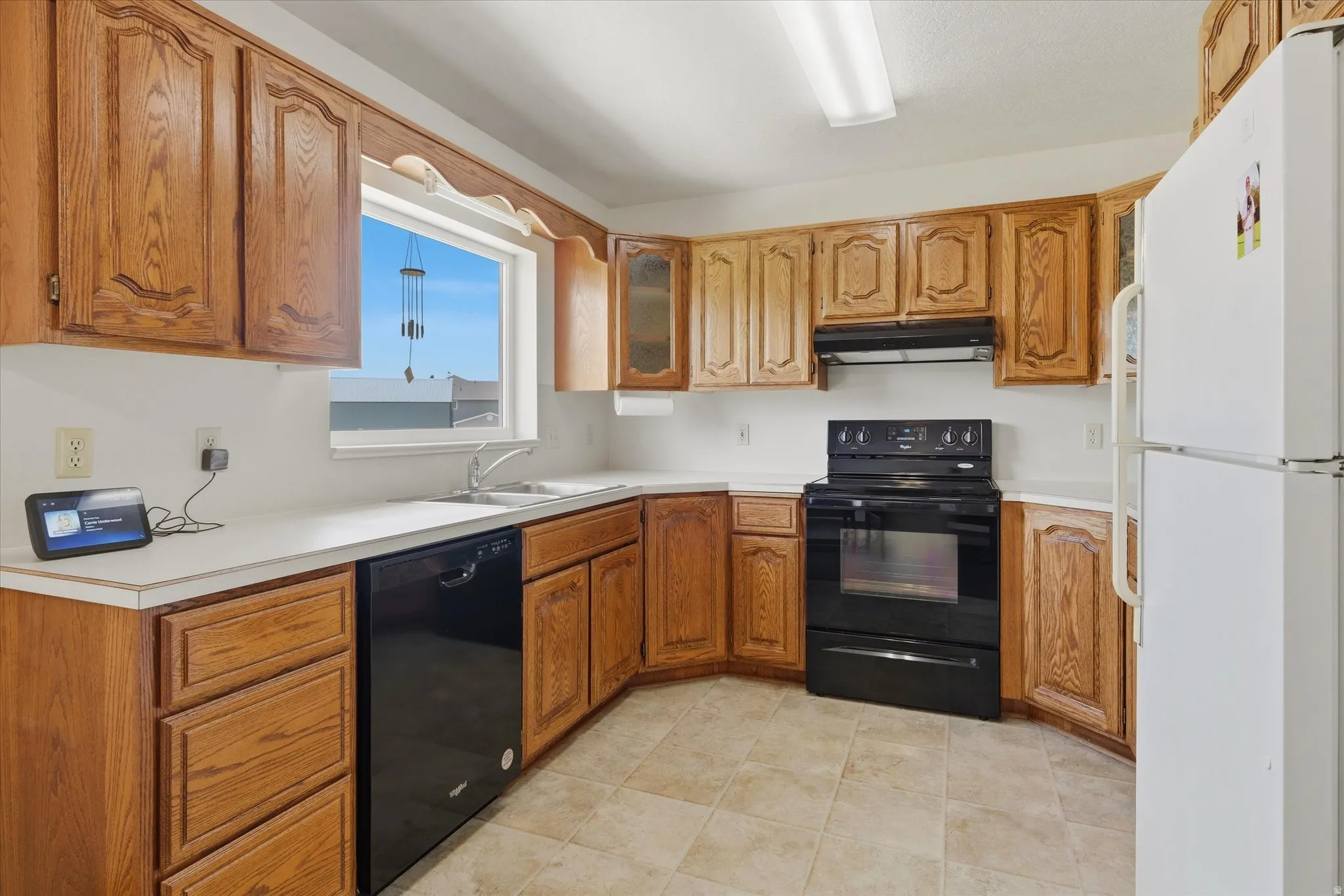 Kitchen featuring wood cabinetry, white countertops, stainless steel sink, black electric range, and black dishwasher