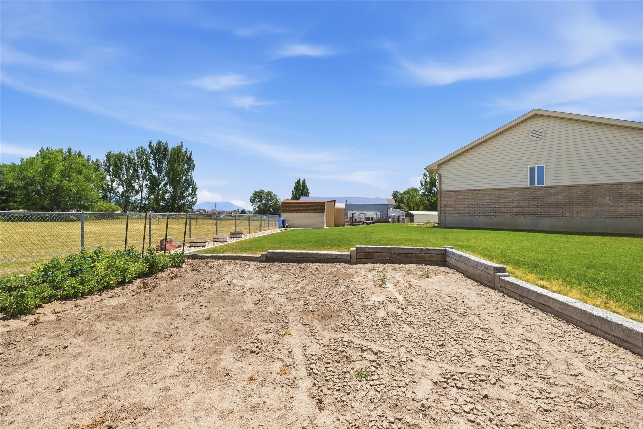 Expansive rear yard featuring a large tilled garden area, a manicured lawn, and a chain-link fence