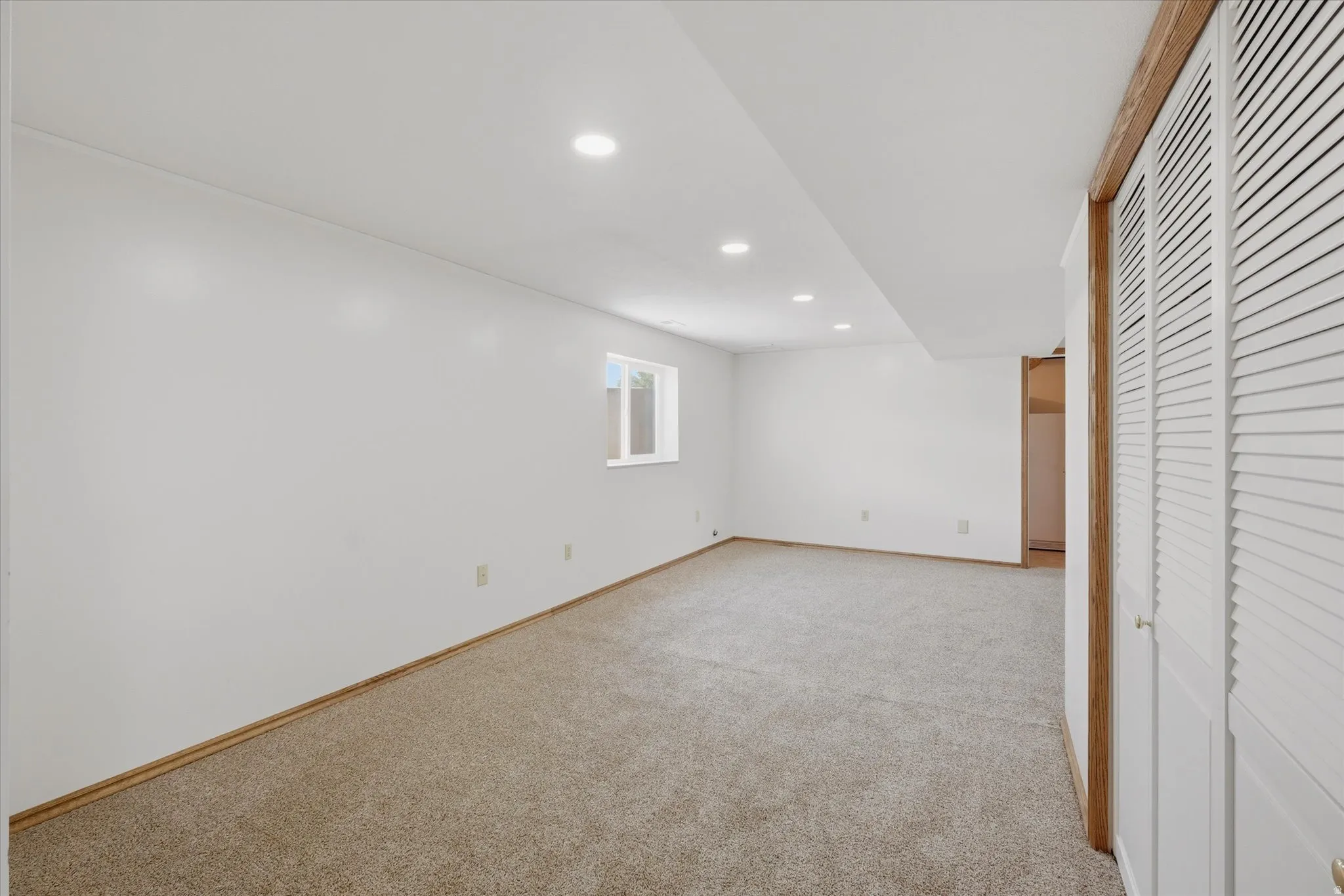 Spacious room featuring neutral carpet flooring, white walls, recessed ceiling lights, and white bi-fold louvered doors