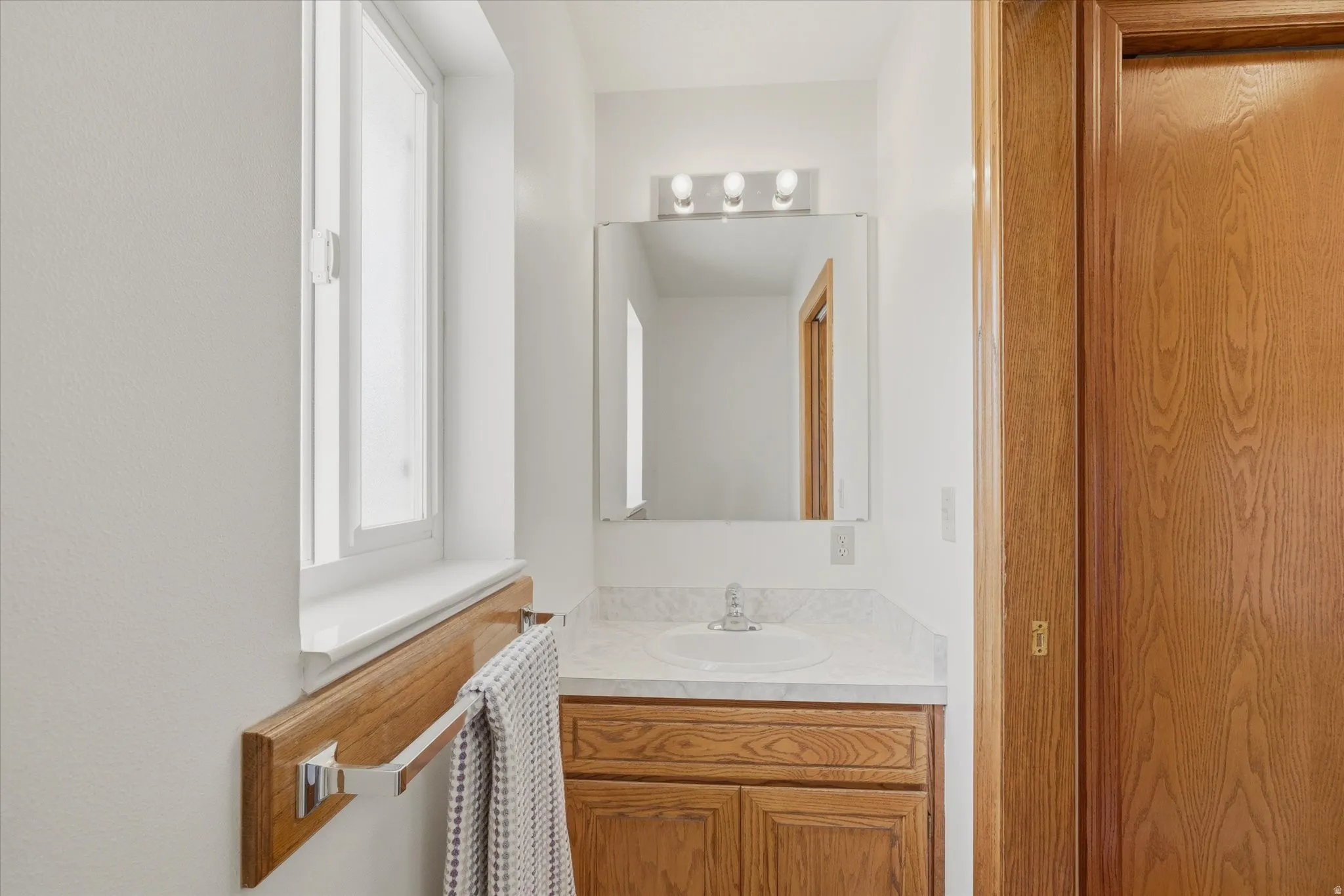 Bathroom vanity with wood-finish cabinetry, a white countertop, and an integrated sink