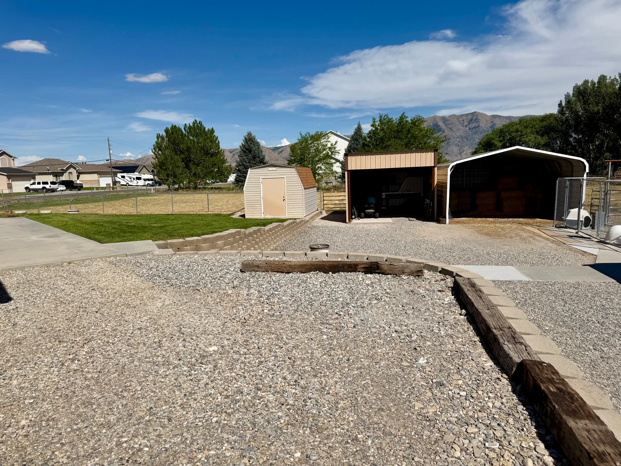 Gravel lot featuring two open-sided structures, a tan storage shed, and concrete paving
