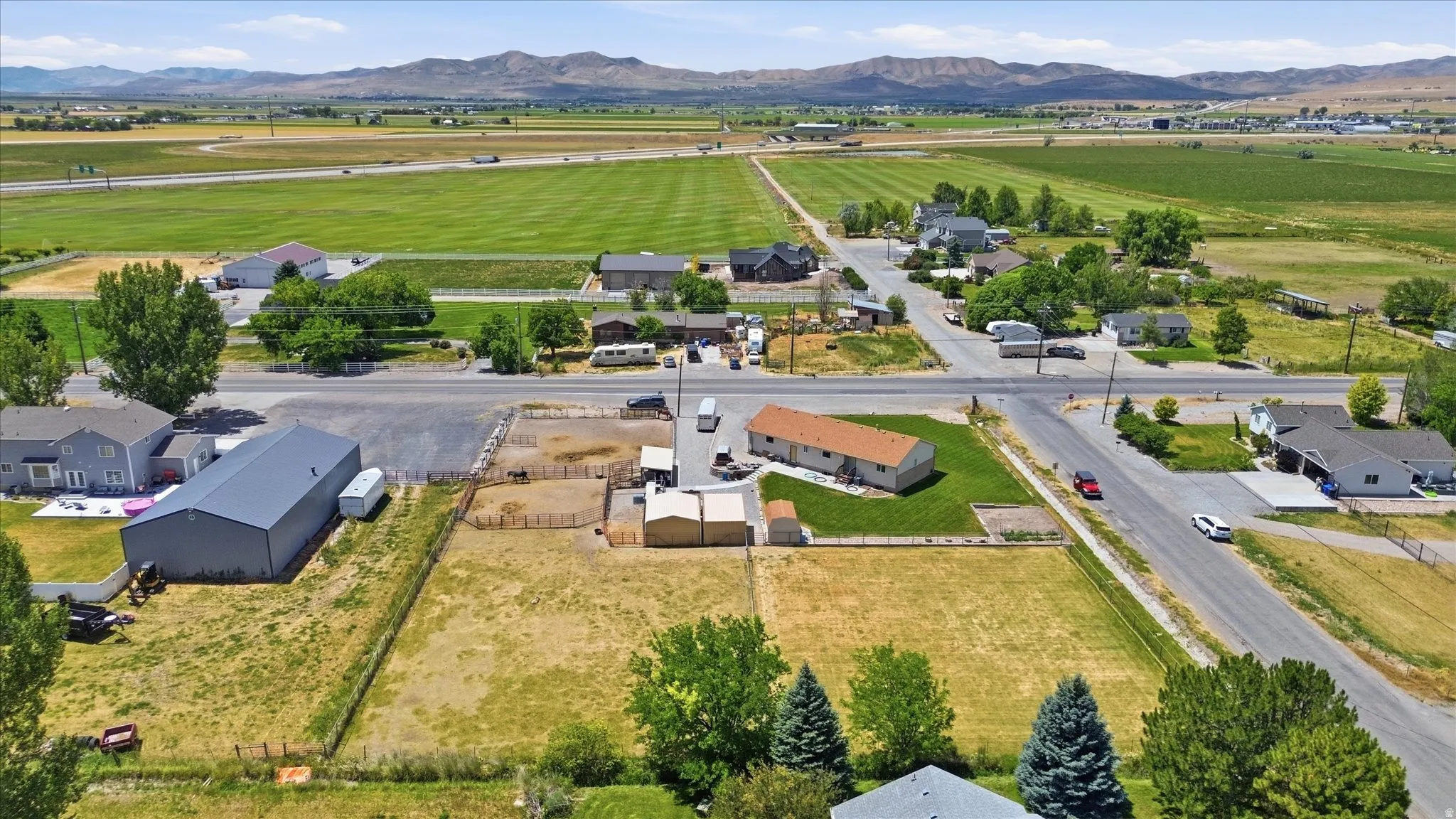 Expansive property featuring a large metal-sided outbuilding, a fenced paddock, and a single-story residence with a brown shingle roof