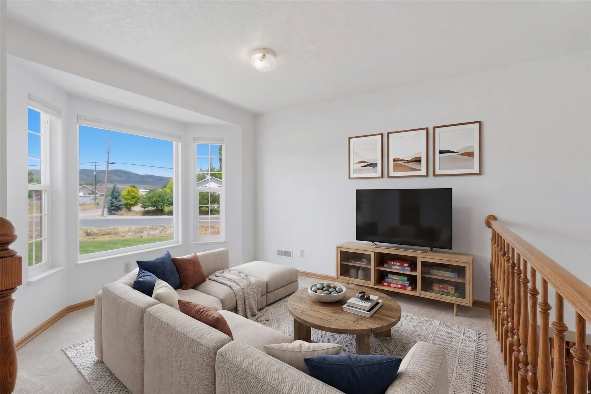 Bright living area featuring a prominent bay window with white trim, a built-in entertainment console with glass-front storage, and light-toned carpet flooring