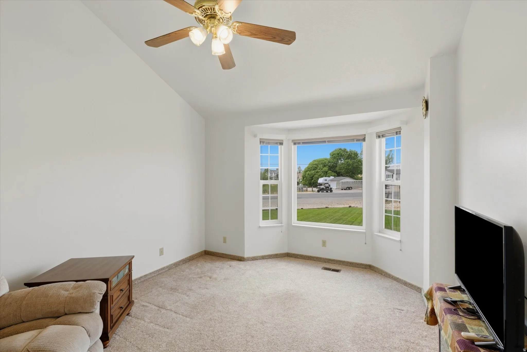 Living area featuring a prominent bay window, vaulted ceiling, and ceiling fan with integrated lighting