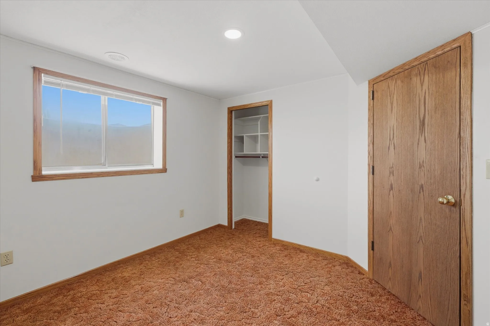 Bedroom featuring a window with wood-trim, a built-in closet with shelving, and a wood-panel door