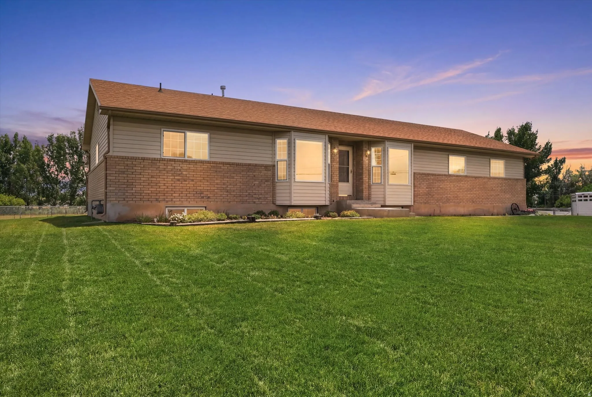 Exterior featuring brick and siding facade, multiple windows, a prominent entrance, a brown shingle roof, and a spacious front lawn