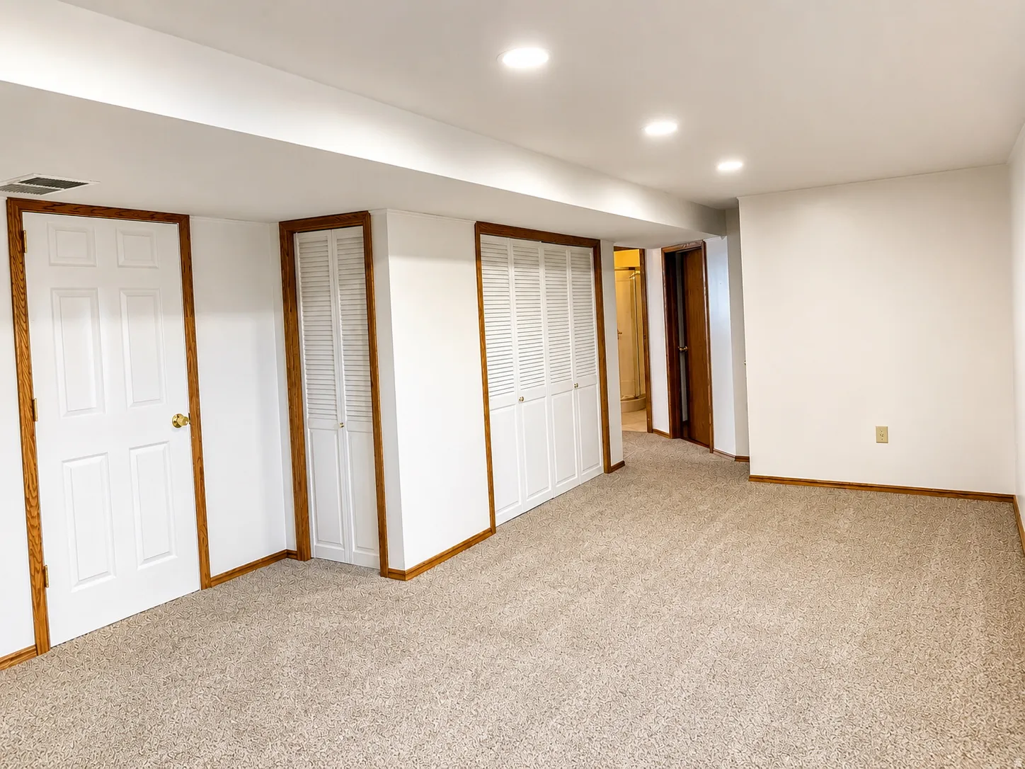 Recessed lighting illuminates the space, featuring neutral carpet flooring and white walls