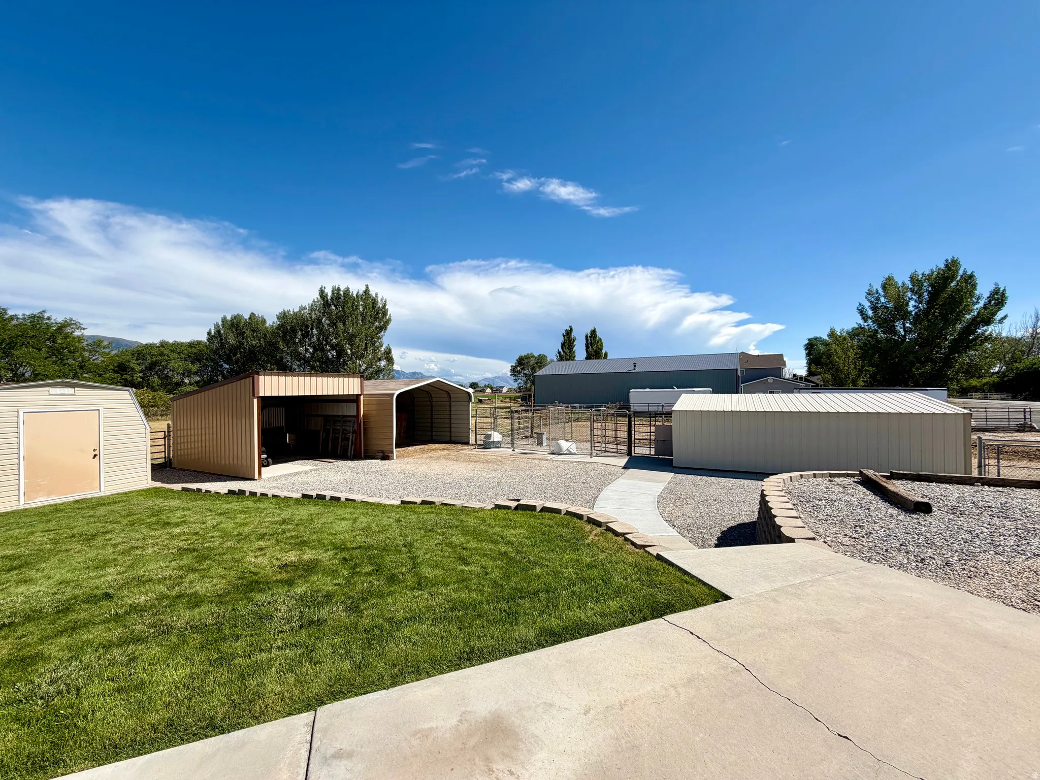 Expansive outdoor space featuring a concrete patio, gravel pathways, a manicured lawn, and multiple utility structures