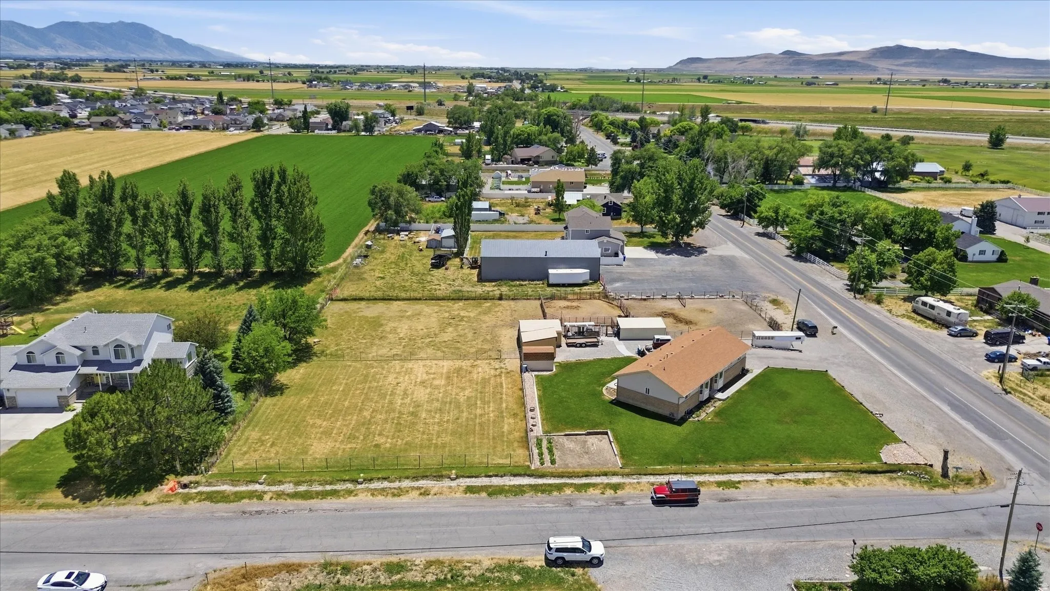 Expansive property featuring a single-story residence with a brown shingle roof and green lawn, accompanied by a substantial adjacent lot