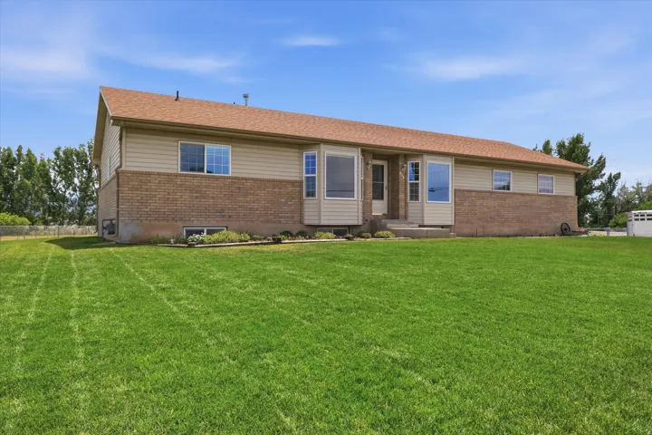 Expansive front lawn with a split-level home featuring a light brown brick facade and beige siding