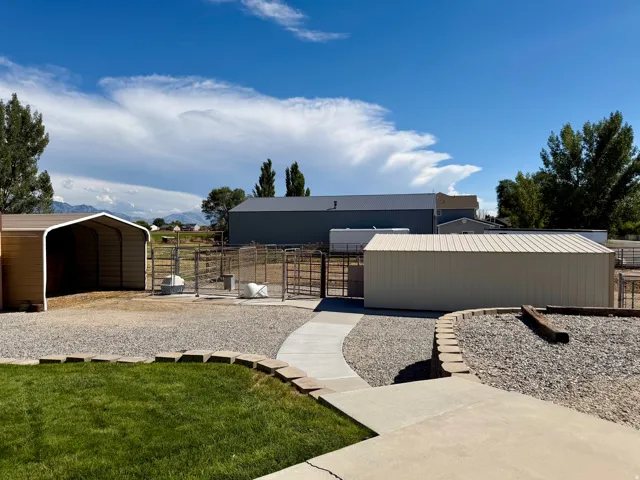 Expansive exterior with a gravel and concrete patio, multiple metal outbuildings, and a grass lawn