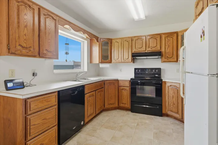 Kitchen featuring wood cabinetry, white countertops, stainless steel sink, black electric range, and black dishwasher