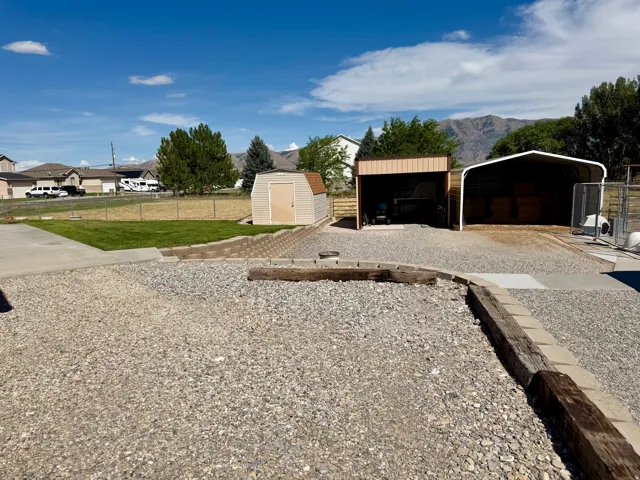 Gravel lot featuring two open-sided structures, a tan storage shed, and concrete paving