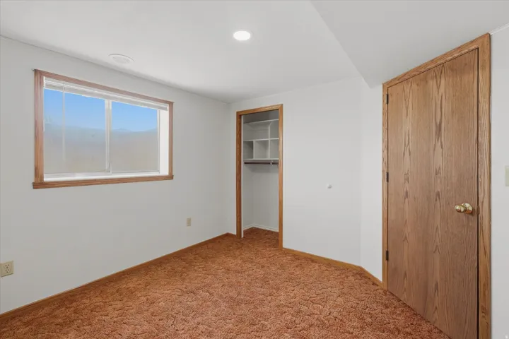 Bedroom featuring a window with wood-trim, a built-in closet with shelving, and a wood-panel door
