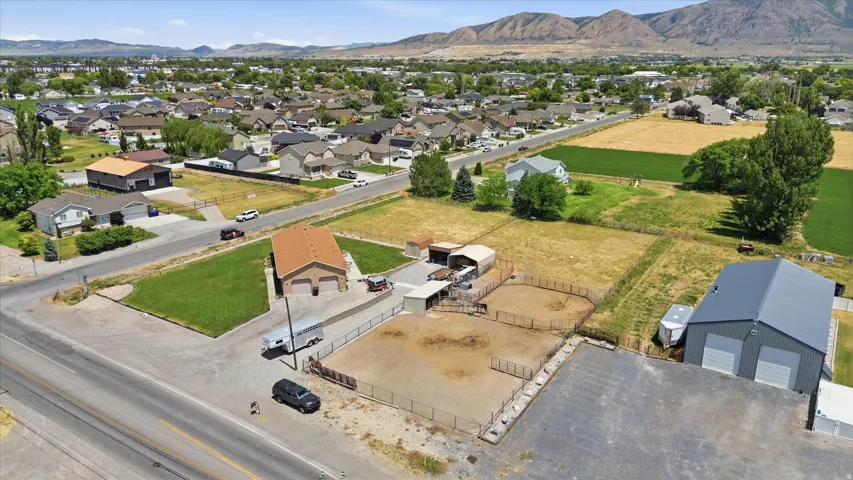 Aerial perspective showcasing a property with a two-story residence featuring an attached garage, a large metal workshop building with dual bay doors, multiple fenced animal enclosures, and substantial land area