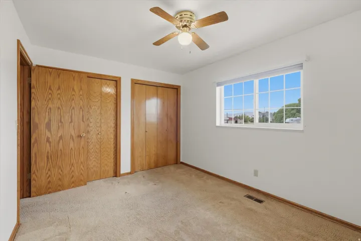 Carpeted interior space featuring a multi-pane window, ceiling fan with light fixture, and two wood-finish bi-fold closet doors