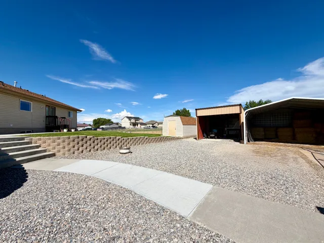 Expansive gravel yard with concrete walkways, a retaining wall, and multiple outbuildings, including a shed and two covered structures