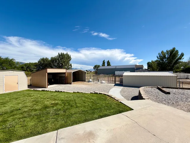 Expansive outdoor space featuring a concrete patio, gravel pathways, a manicured lawn, and multiple utility structures