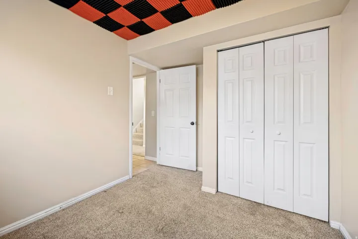 Room featuring neutral carpet flooring, light beige wall paint, a bi-fold closet with panel doors, and a ceiling with black and orange acoustic panels