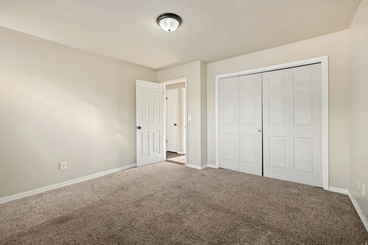 Carpeted room featuring a neutral wall palette, white trim, a semi-flush mount ceiling light, and bi-fold closet doors