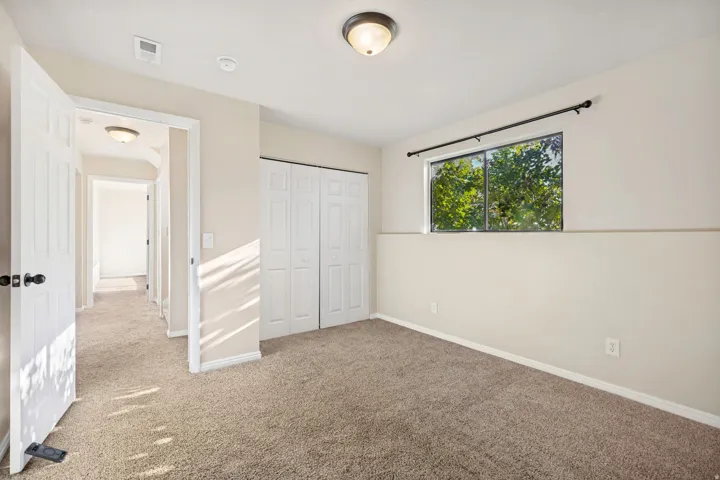 Carpeted room featuring a double bi-fold closet, a window with a dark curtain rod, and a flush-mount ceiling light