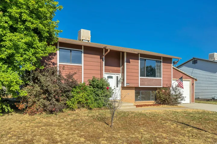 Split-level residence featuring a brown siding exterior, attached garage, white entry door, and mature landscaping